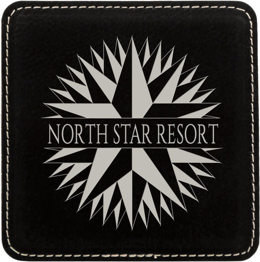 Black and silver square leatherette coaster engraved with a resort compass logo